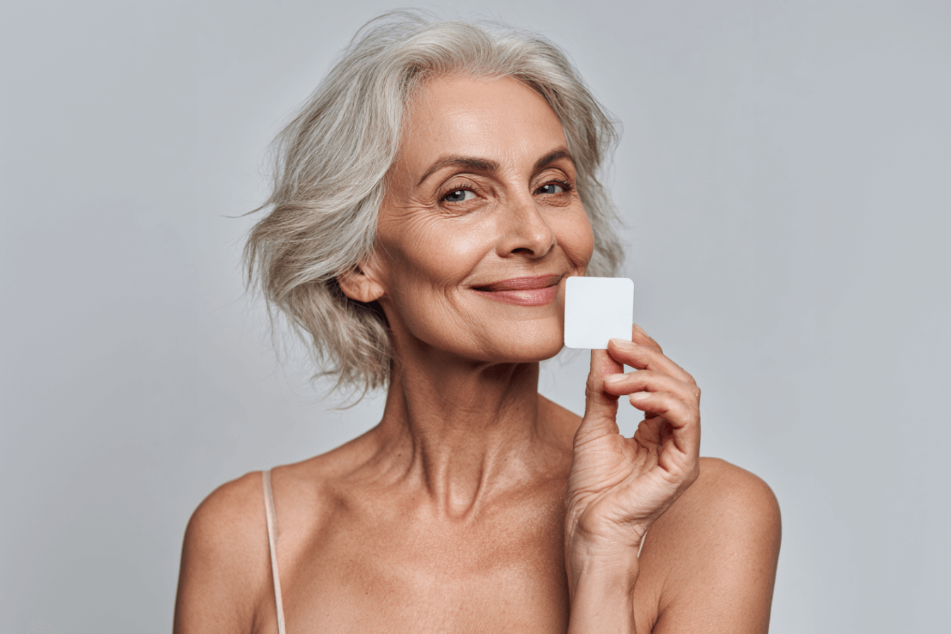Smiling woman holding a small white square against her face.