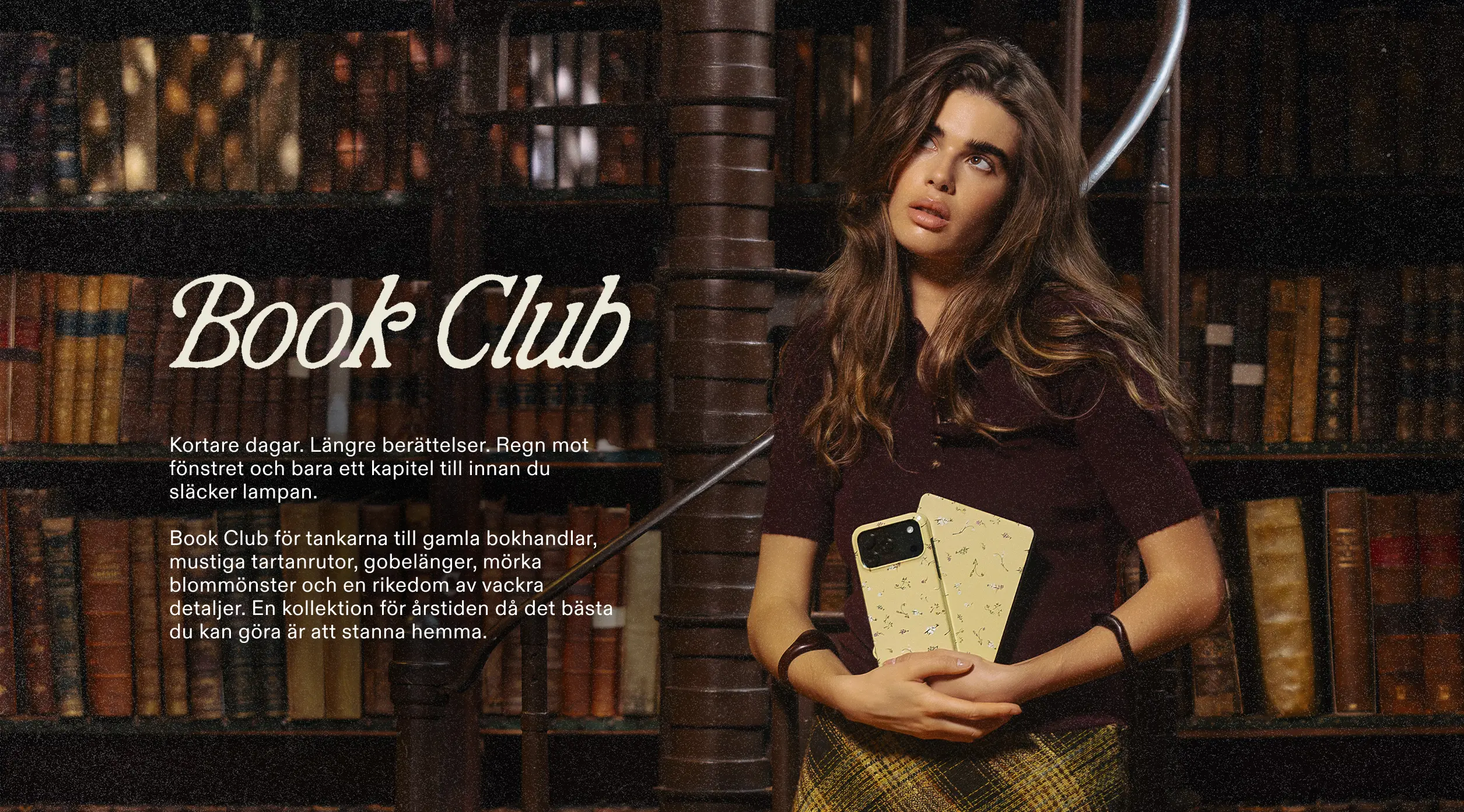 A woman stands in a library holding two yellow, patterned phone cases while looking up and to the side.