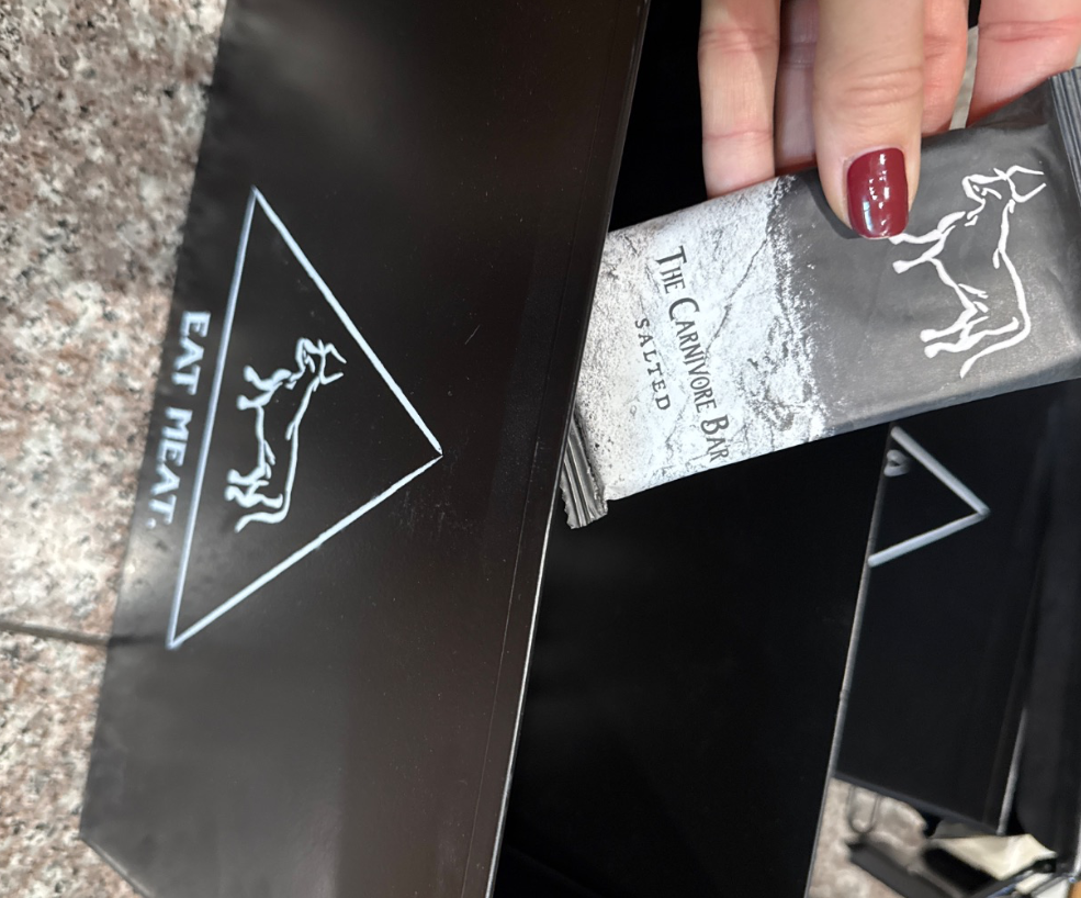 A hand with red nail polish pulling a salted Carnivore Bar from a black display box.