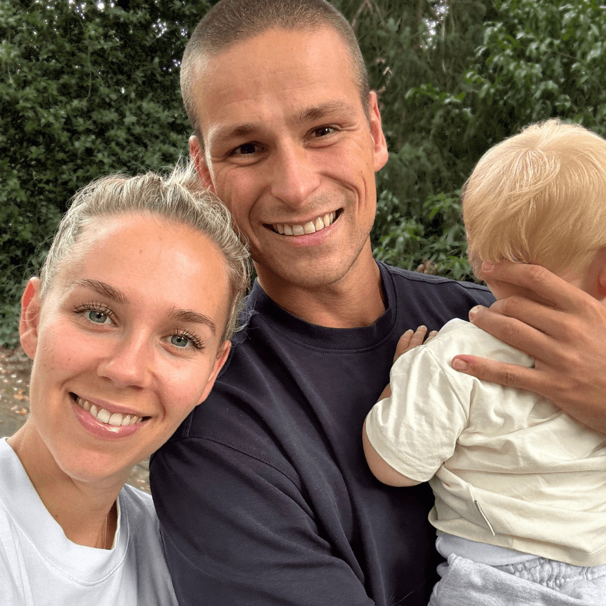 A smiling man and woman pose for a photo as the man holds a small child.