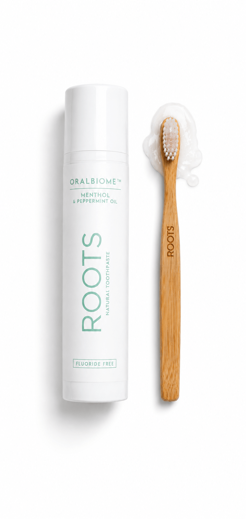 A white tube of ROOTS natural toothpaste next to a bamboo toothbrush with toothpaste on its bristles.