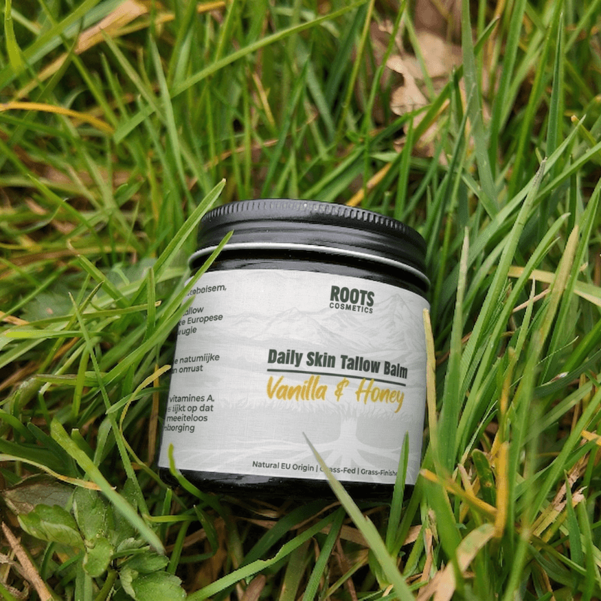 A jar of Roots Cosmetics Daily Skin Tallow Balm, Vanilla & Honey, sits in lush green grass.
