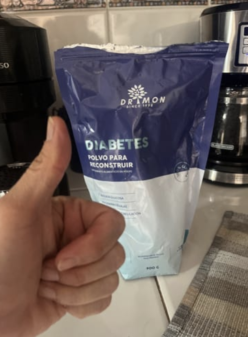 Thumbs up in front of a dietary product package on a kitchen counter.