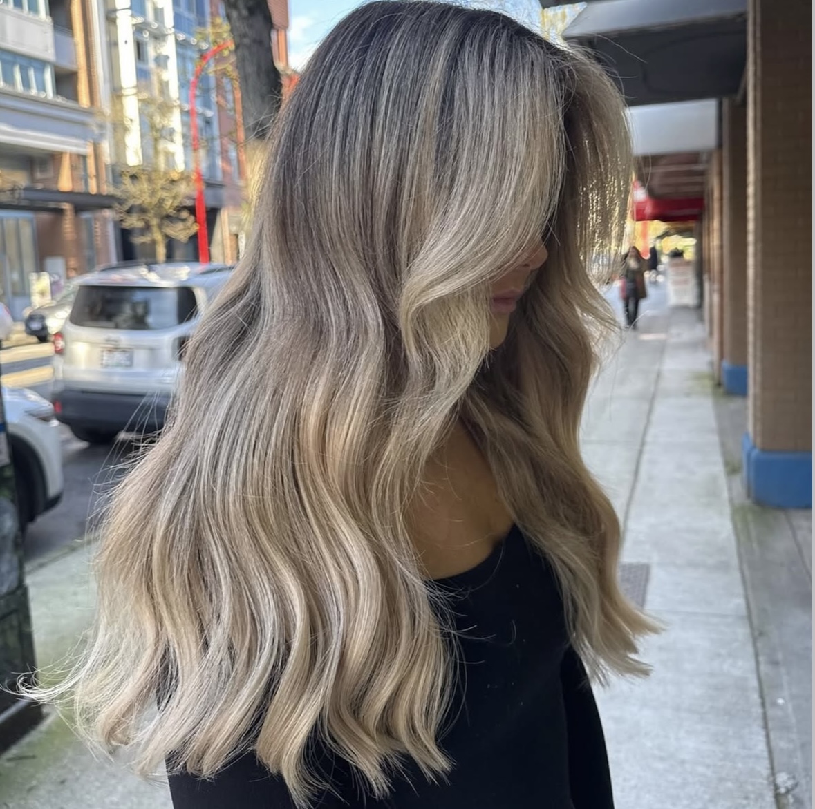 Person with long, wavy blonde hair standing on a city sidewalk.