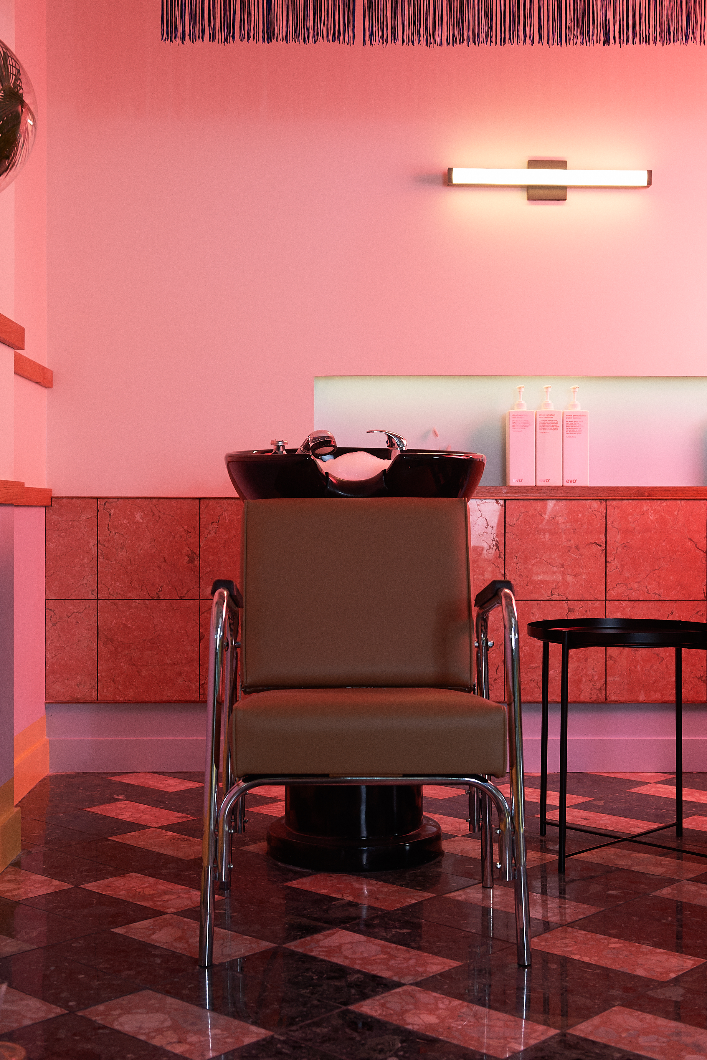 Salon chair and sink in a modern, pink-lit room.