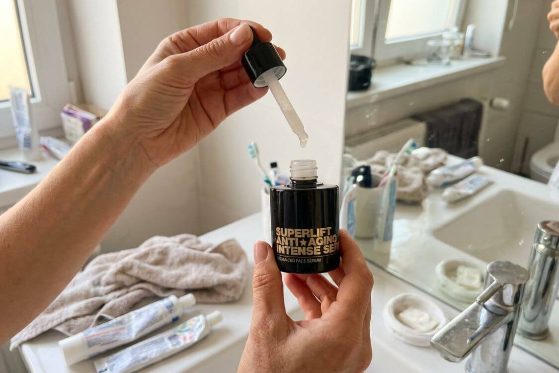 A person holds an open bottle of face serum and a dropper in a bathroom.
