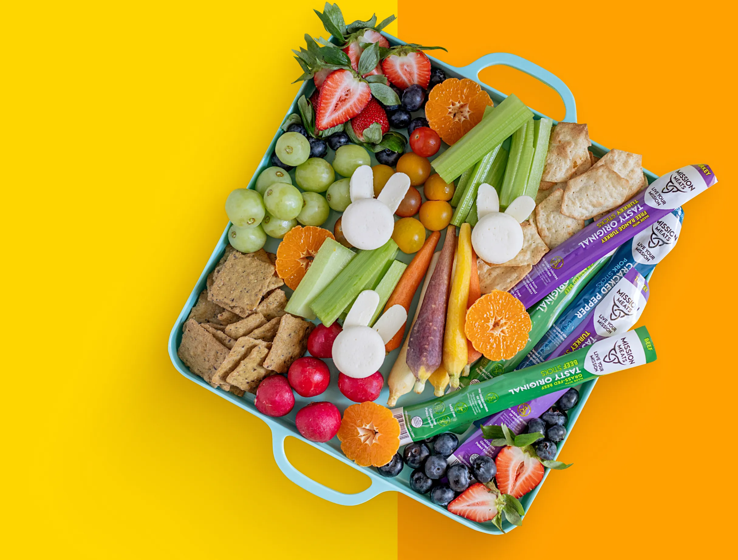 Colorful platter with fruits, vegetables, crackers, and cheese on a yellow and orange background.