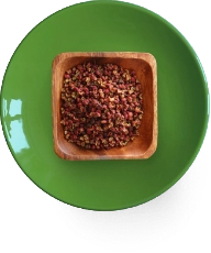 Wooden bowl with red peppercorns on a green plate.