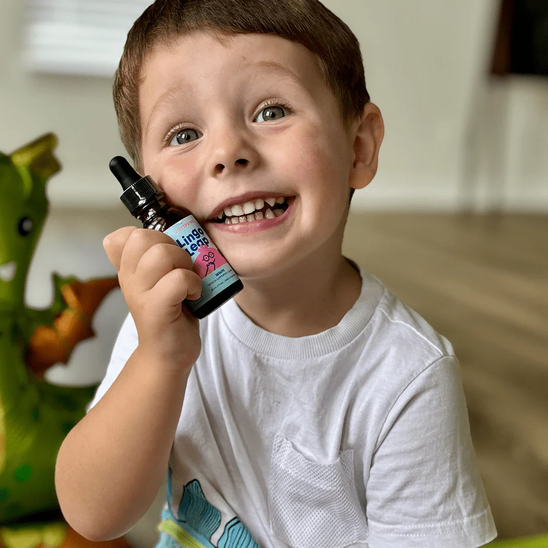 Child smiling, holding a small bottle, with a green toy dinosaur in the background.