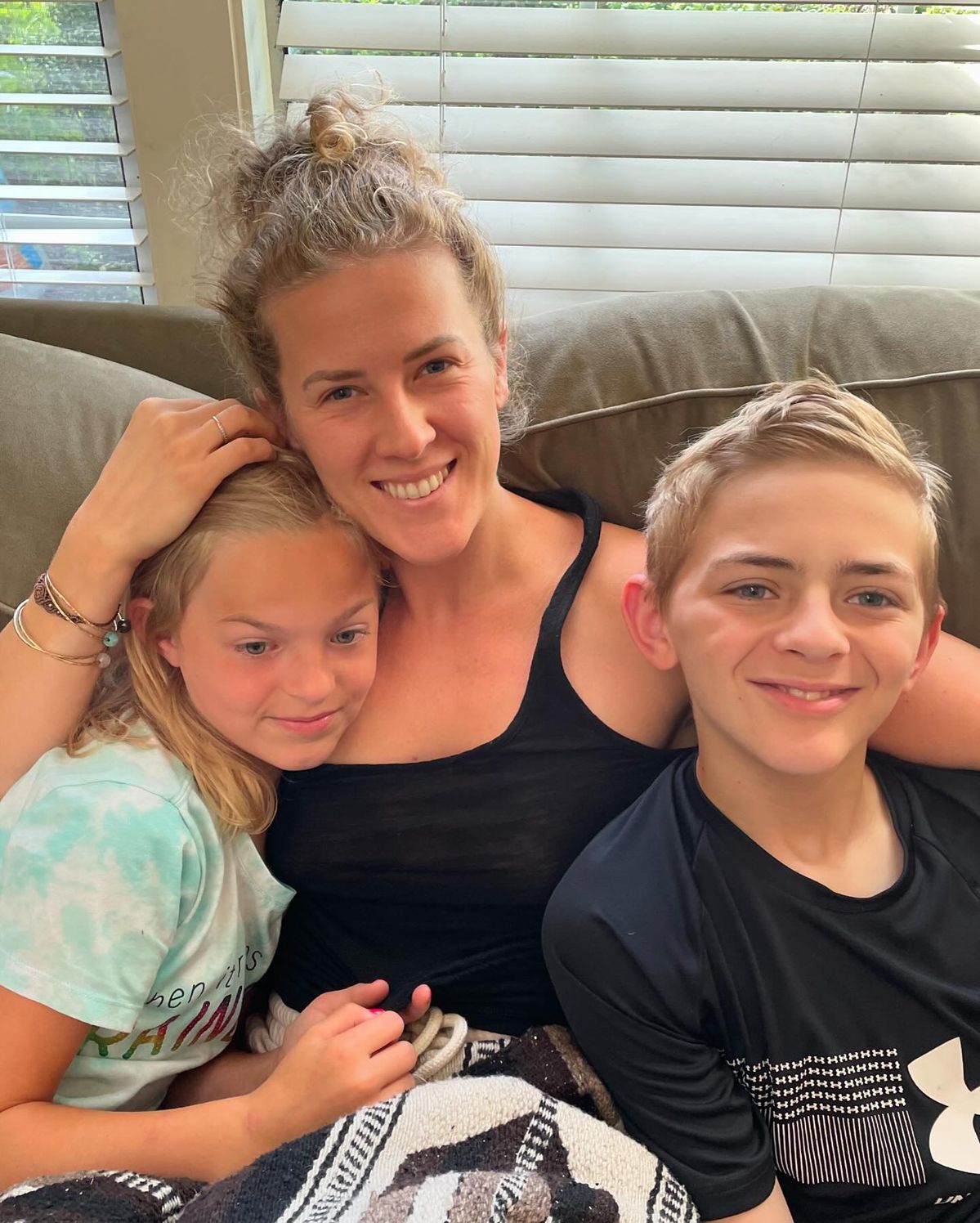 A woman sits on a couch between a young girl and a young boy, all smiling at the camera.