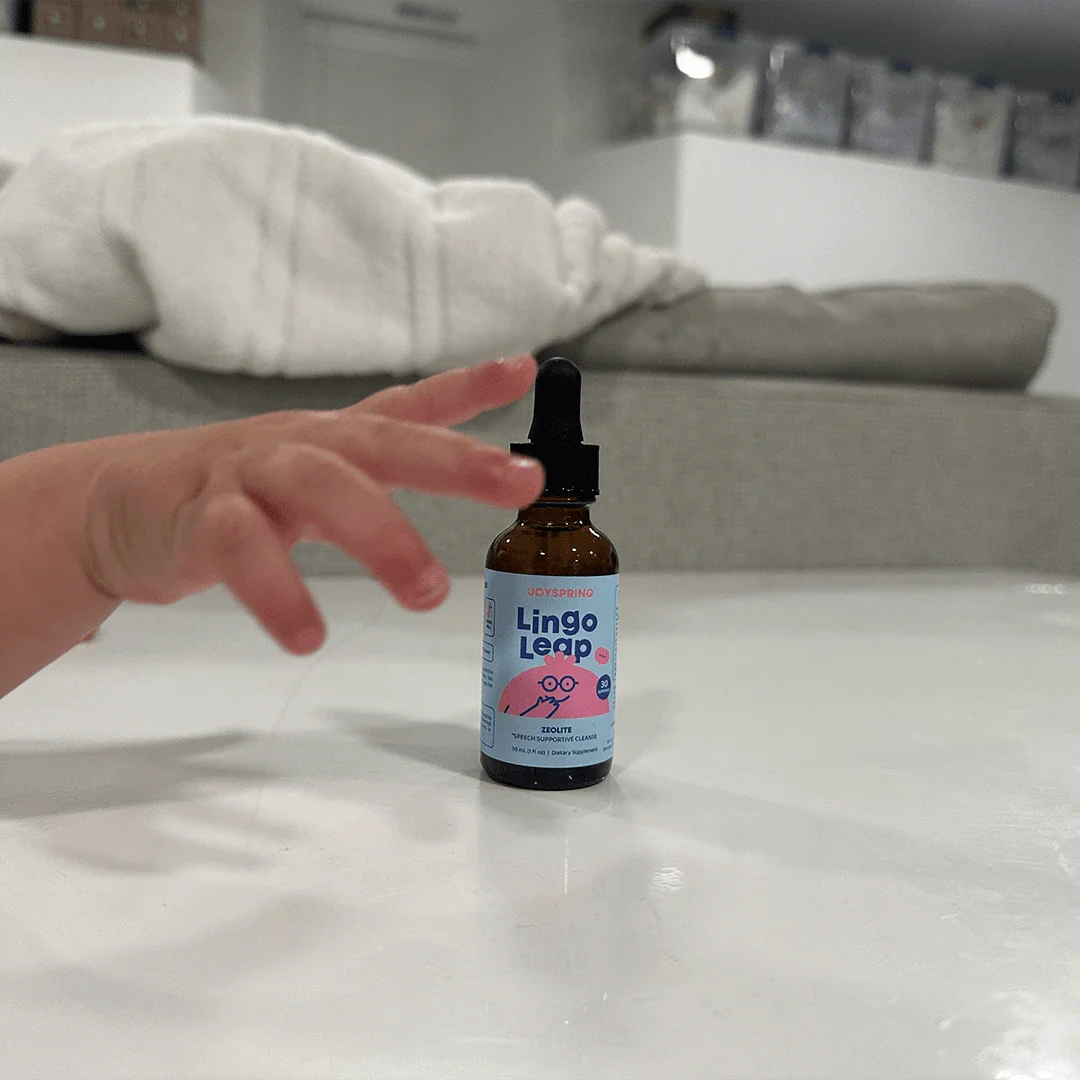 Child's hand reaching for a bottle of Lingo Leap on a table.