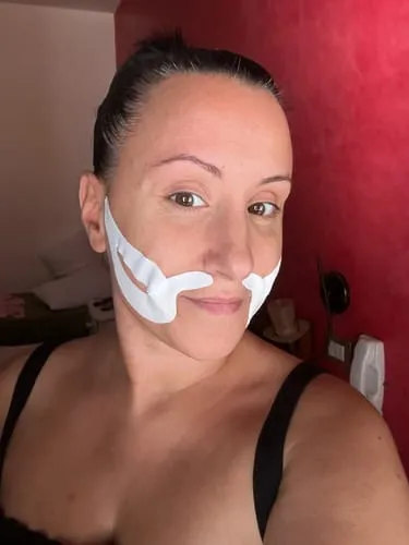 A woman with dark hair pulled back looks at the camera with white tape on her face.