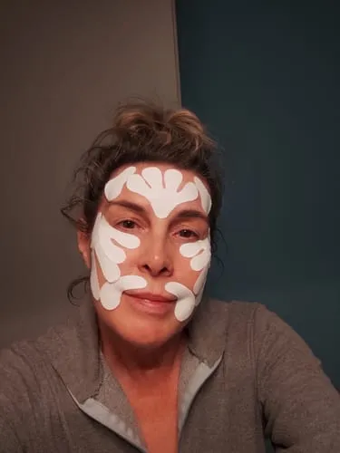 A woman with white, patterned tape on her face, including her forehead, cheeks, and around her mouth.