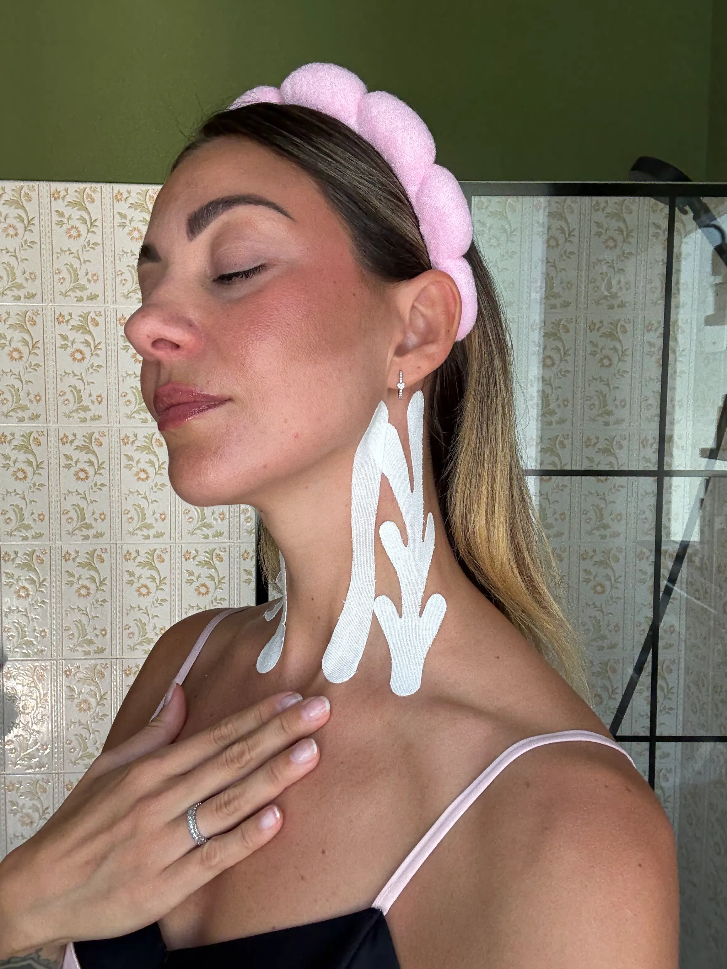 A woman with her eyes closed wears a pink headband and has white therapeutic tape on her neck.