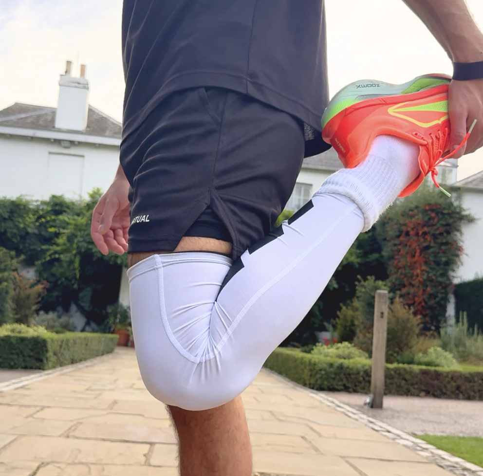 Person stretching leg wearing white leggings and bright shoes on a paved path.