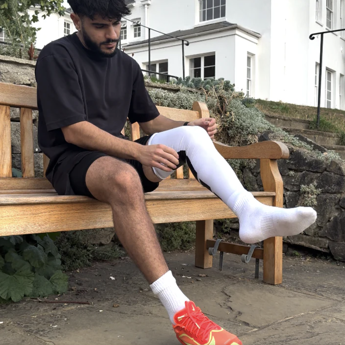 Man sitting on a bench adjusting his pant leg outdoors.