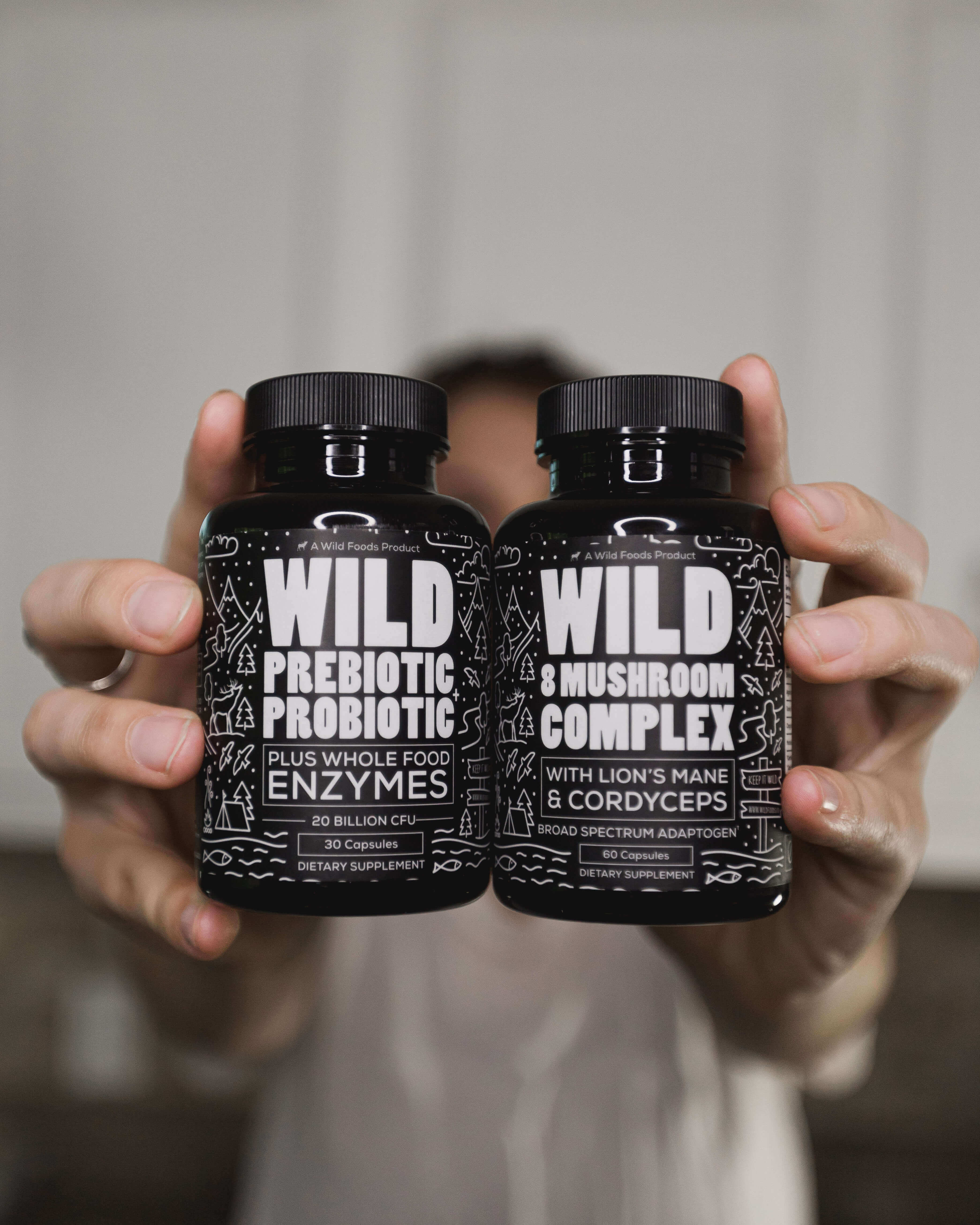 Two supplement bottles labeled 'Wild Prebiotic Probiotic' and 'Wild Mushroom Complex' held in hands.