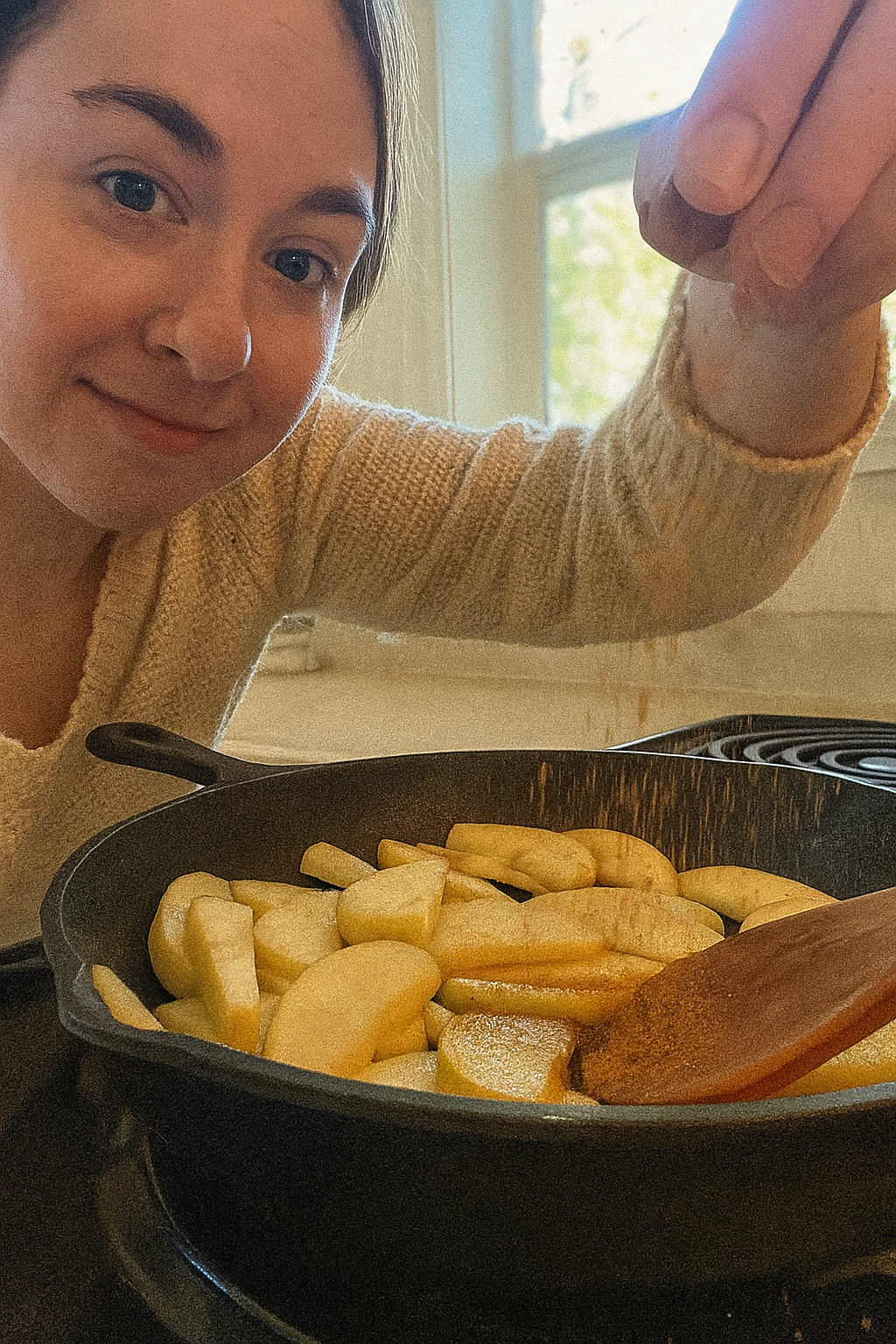 Person cooking sliced apples in a pan on a stove.