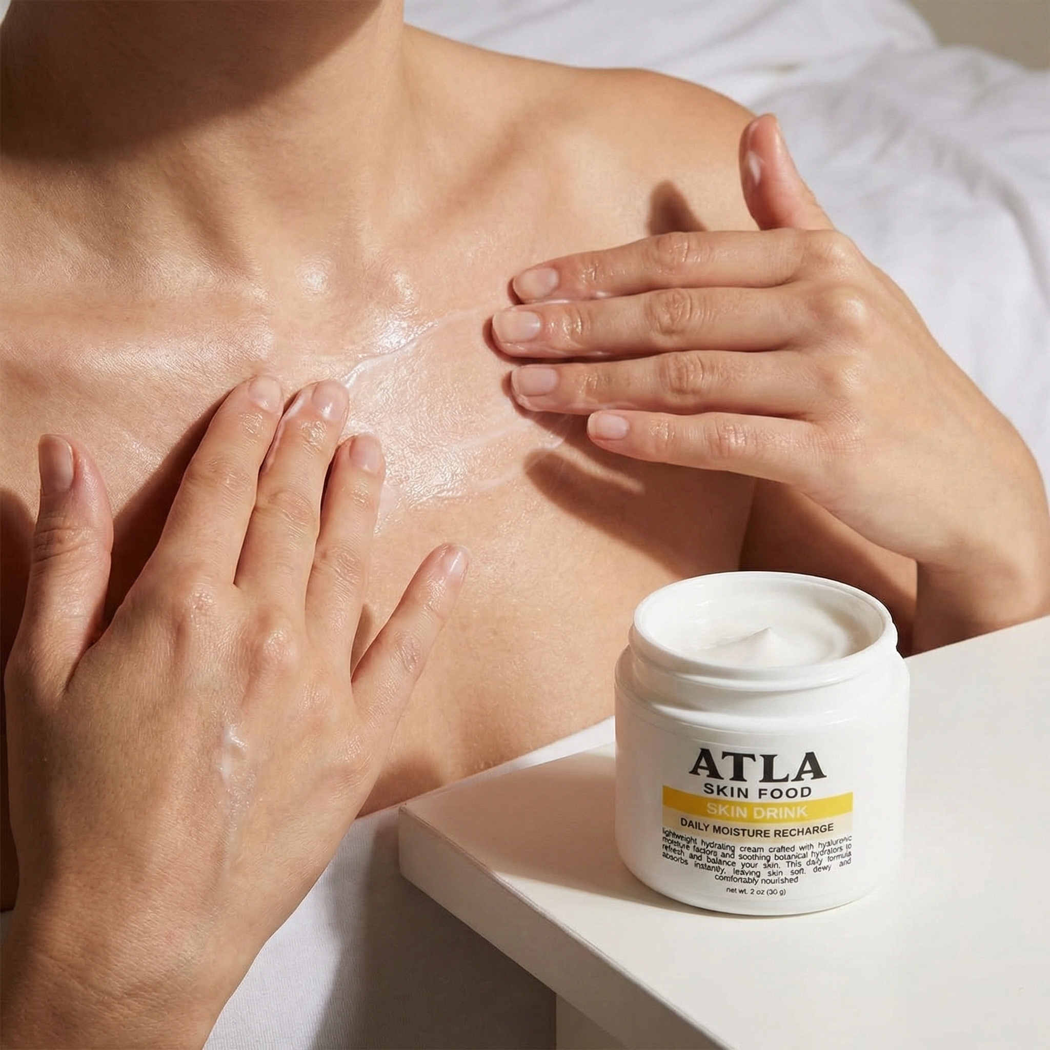 A person applies a white cream to their chest, with a jar of ATLA Skin Food lotion nearby.