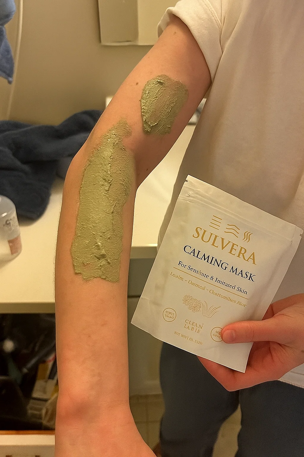 Person applying green mask on arm, holding Sulvera Calming Mask packet.
