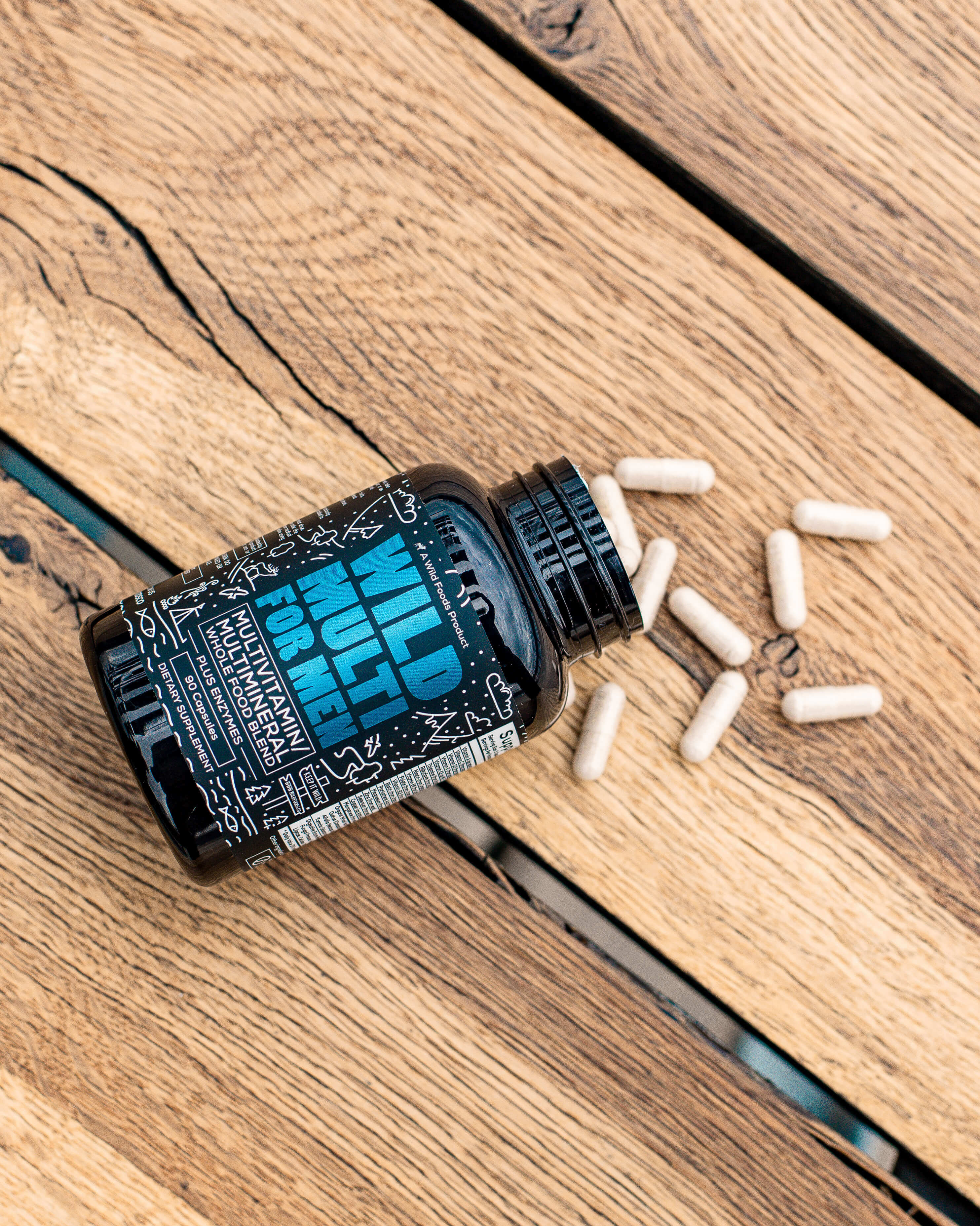 Black bottle labeled 'Wild Multi' with capsules on wooden surface.