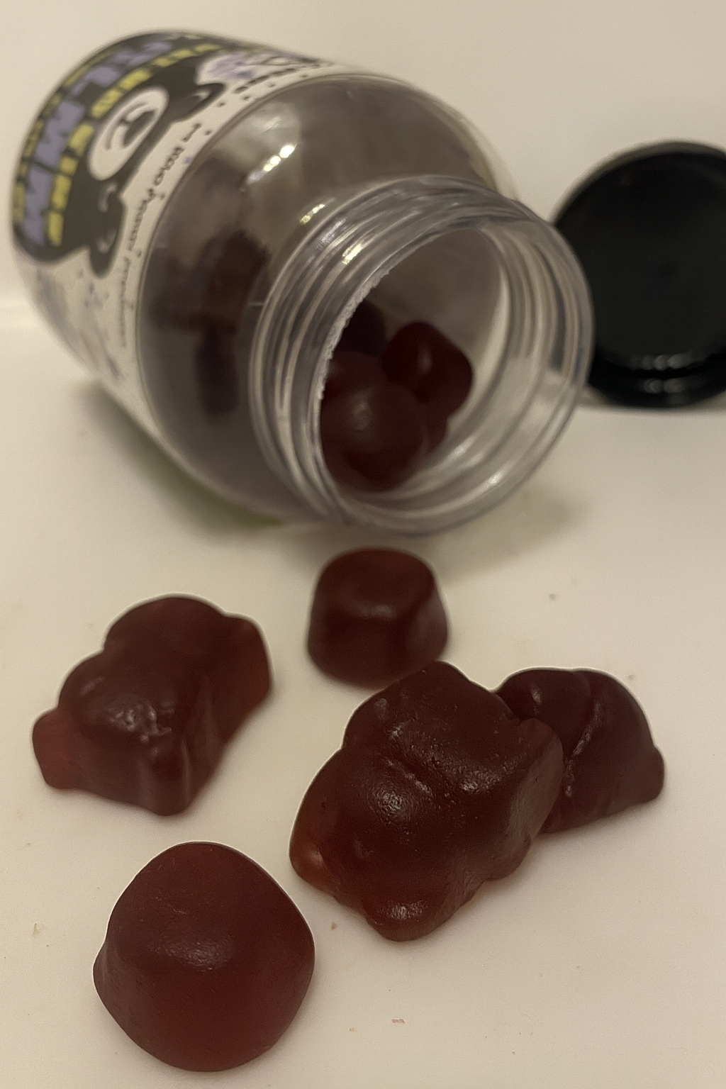 Open jar with gummy bears spilling out on a white surface.