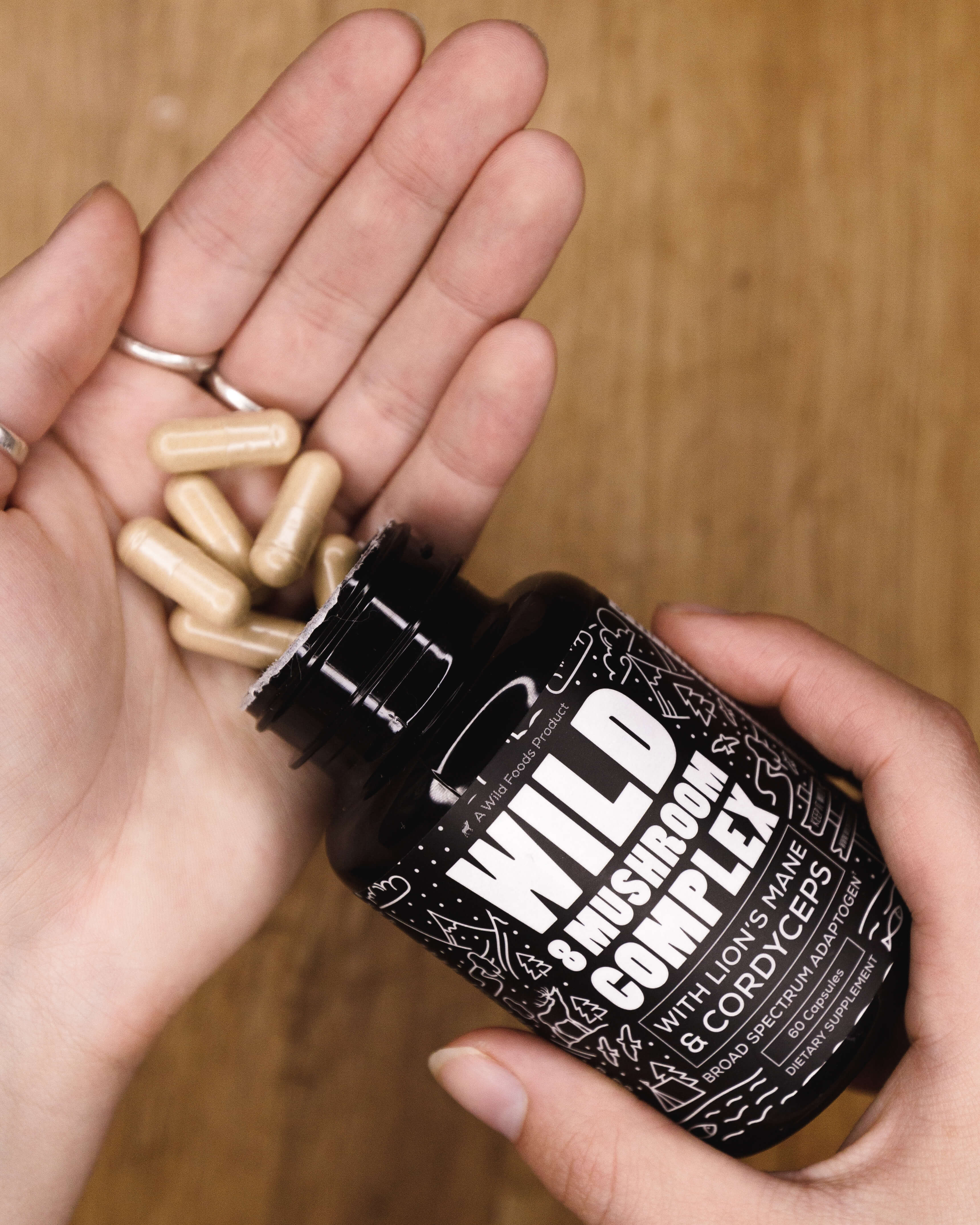 Hand holding a bottle of 'Wild 8 Mushroom Complex' and capsules.