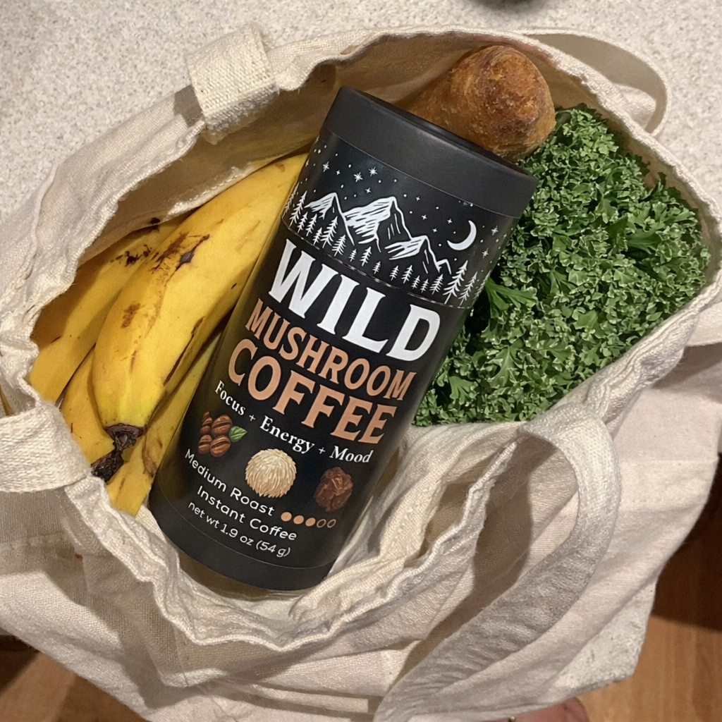 Tote bag with bananas, wild mushroom coffee, baguette, and green leafy vegetables.