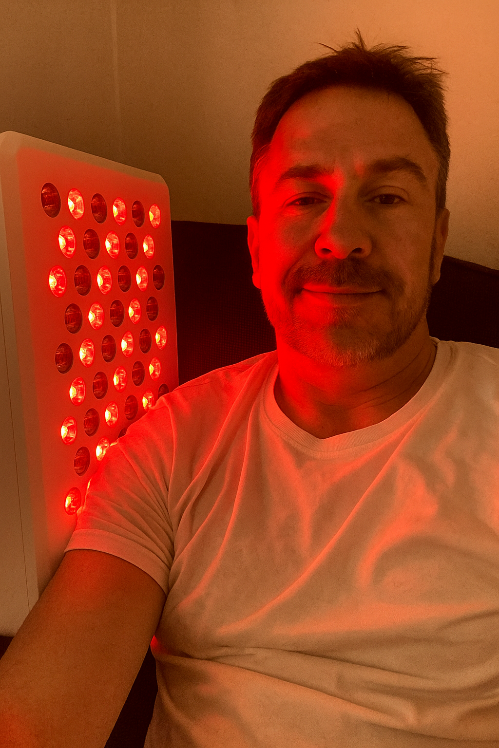 Person in a white shirt next to a red light therapy device.