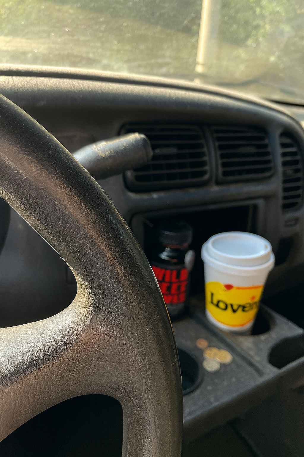 Car dashboard with steering wheel, coffee cup, and supplement bottle.