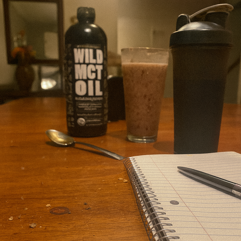 Notebook, pen, spoon, drink, and MCT oil bottle on a wooden table.