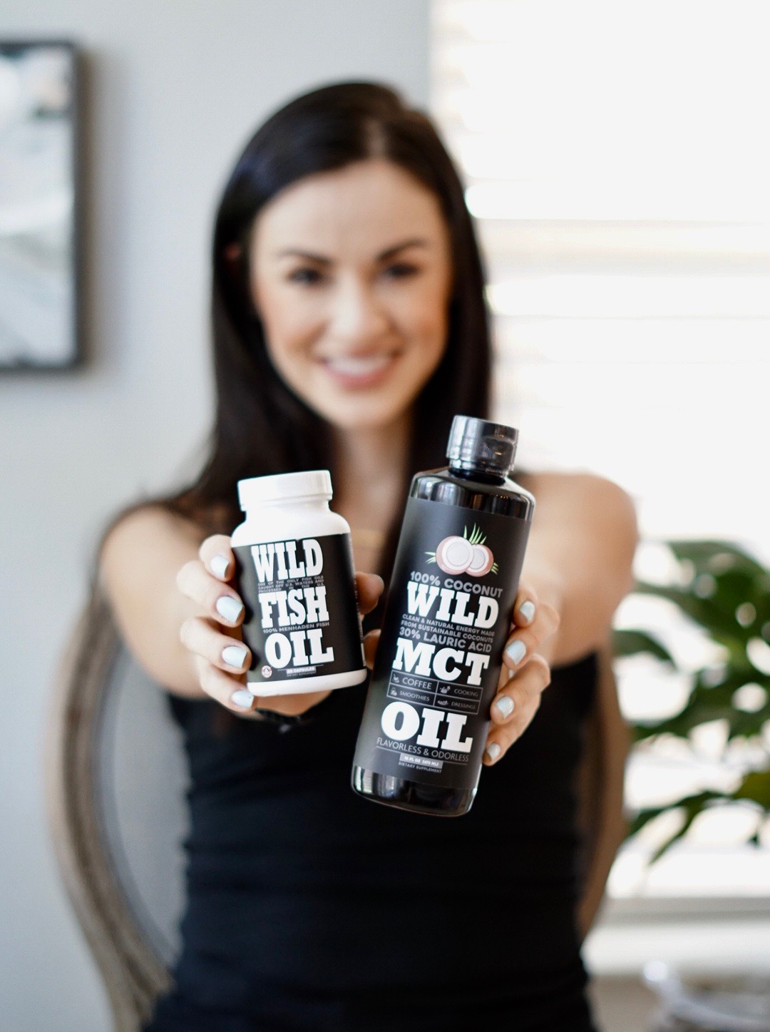 A person holding Wild Fish Oil and MCT Oil bottles.