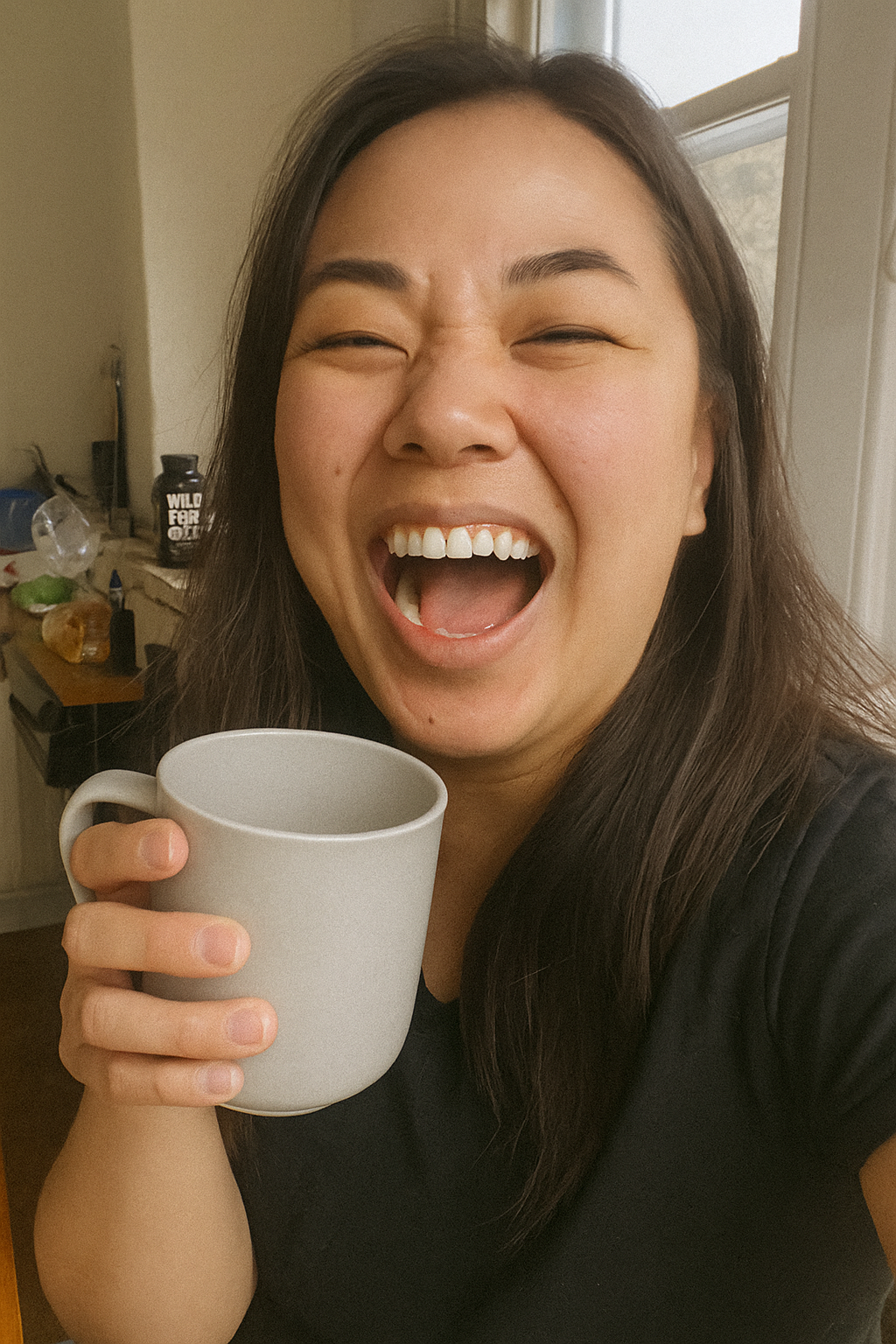 Person laughing while holding a mug indoors.