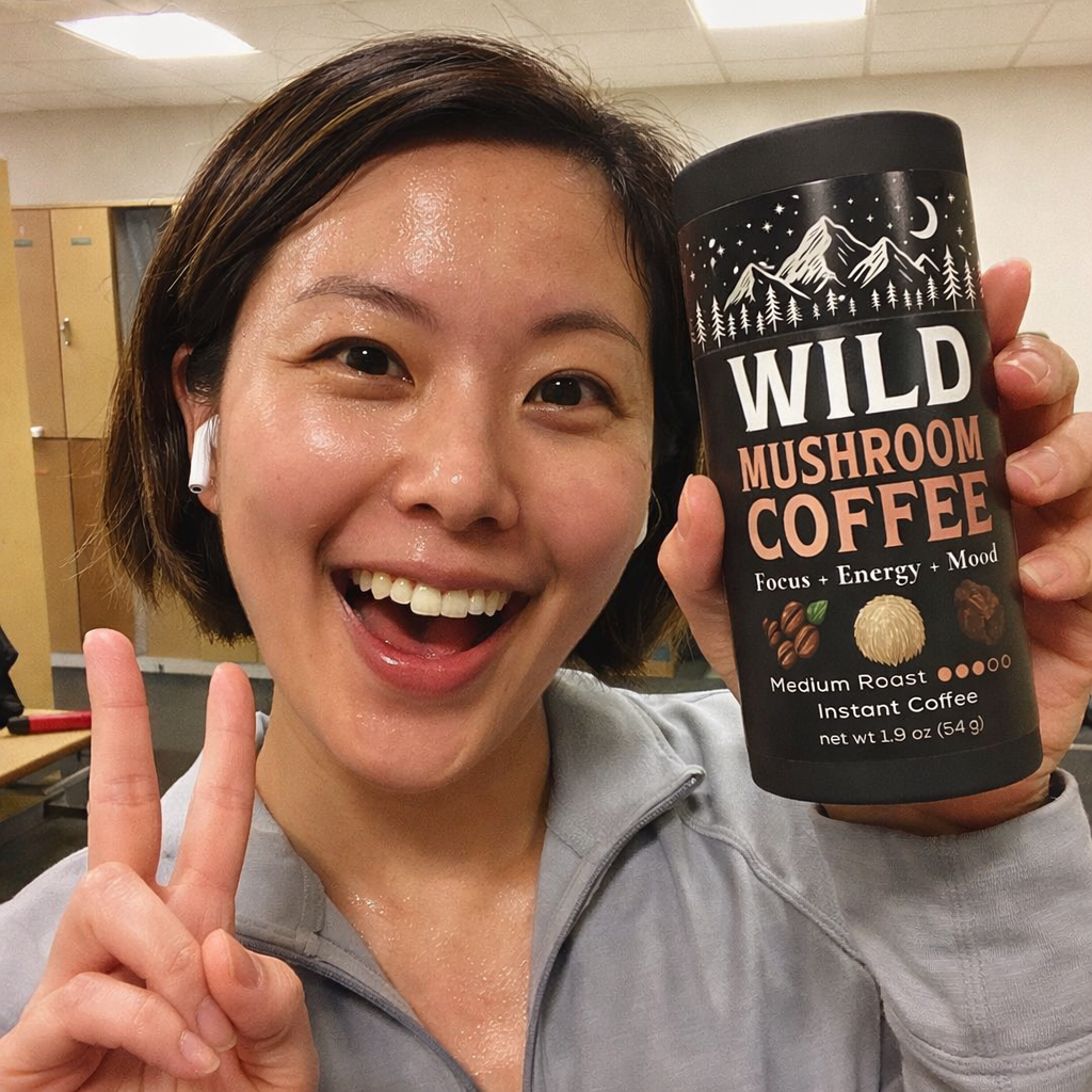 Person smiling holding a container of Wild Mushroom Coffee, showing a peace sign.