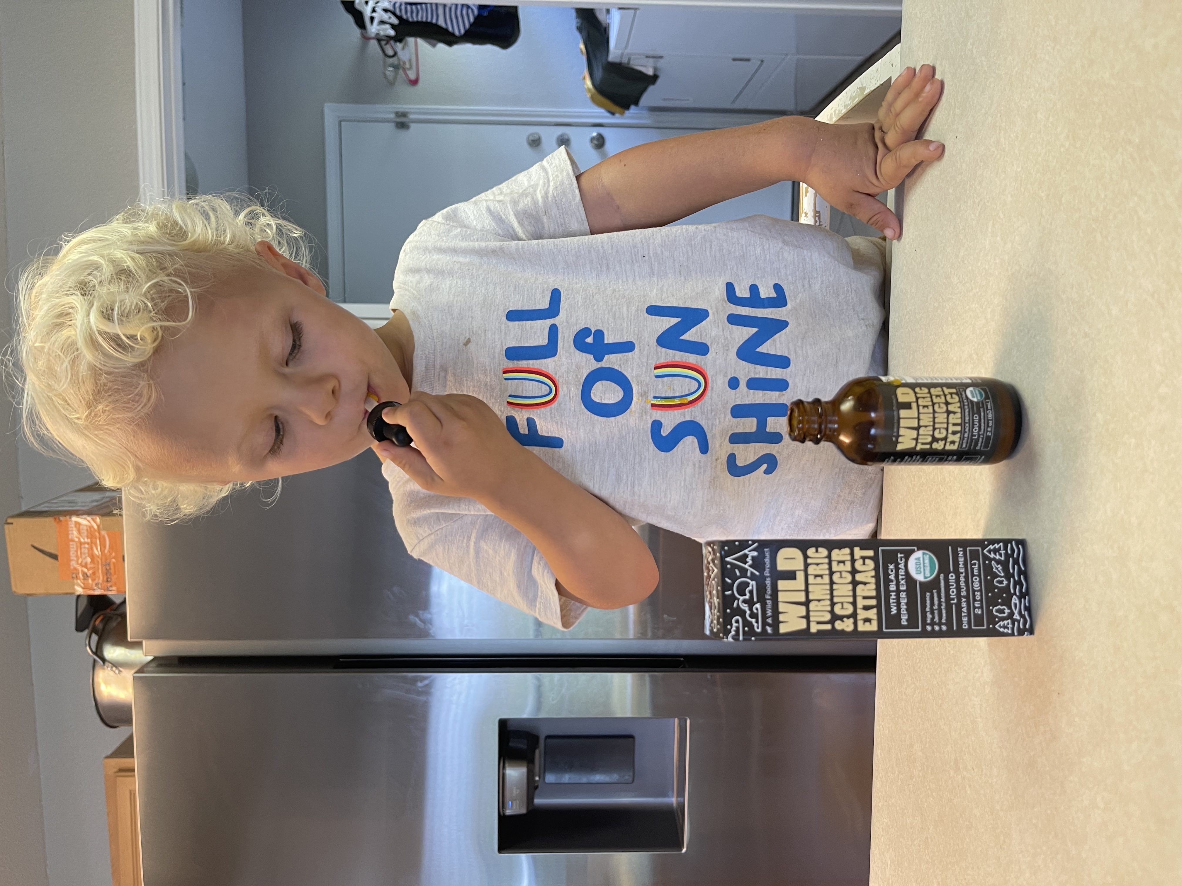 Child in 'Full of Sunshine' shirt holds dropper near turmeric extract bottle.