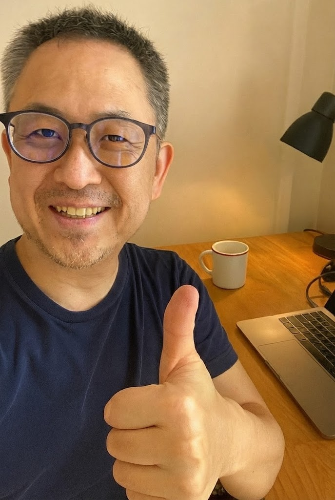 Person giving a thumbs-up in front of a desk with a laptop and mug.
