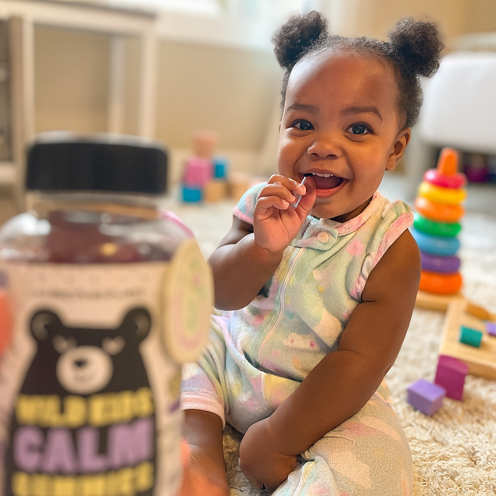 Smiling child with toys, holding a gummy; bottle in foreground.
