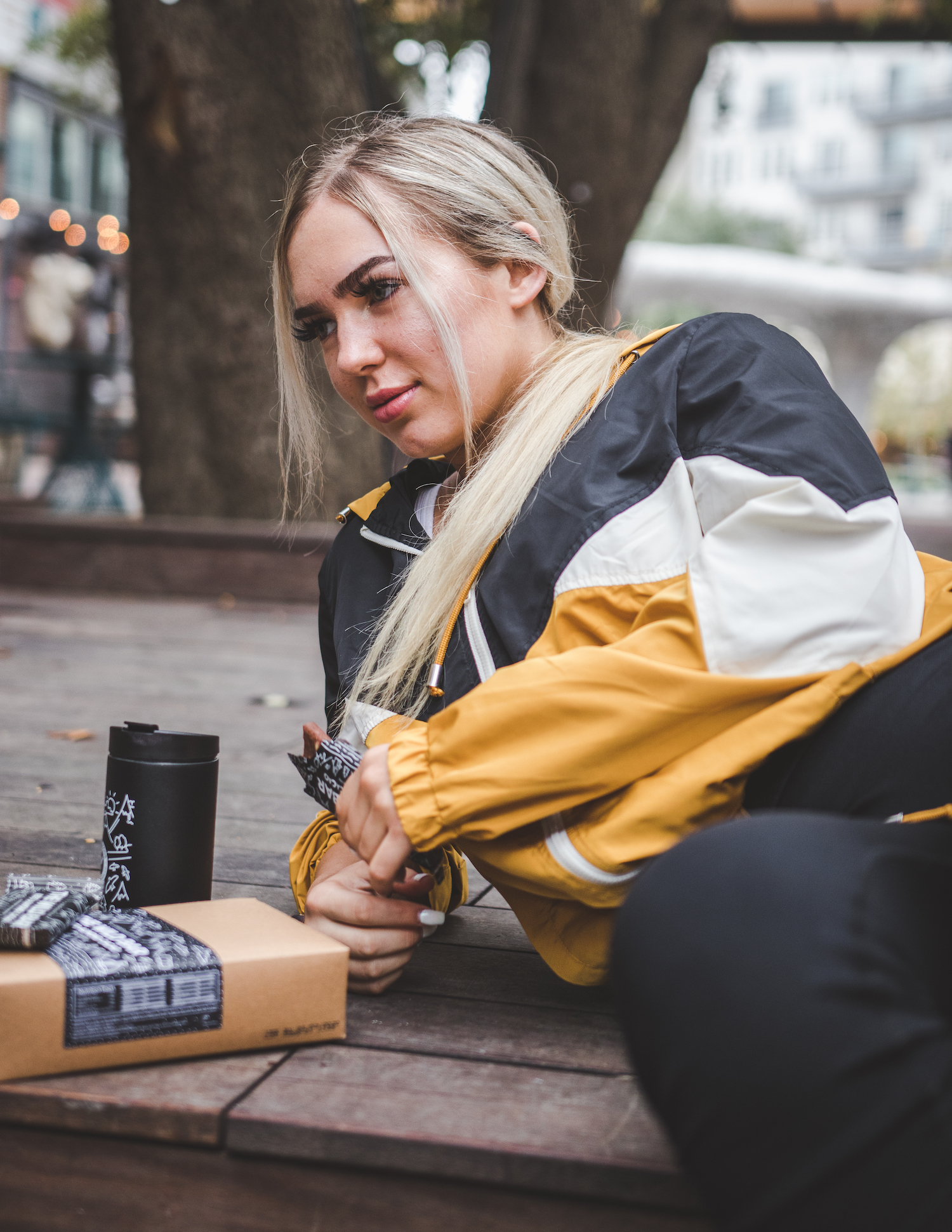 Person in a yellow jacket sitting outdoors with a snack and coffee cup.