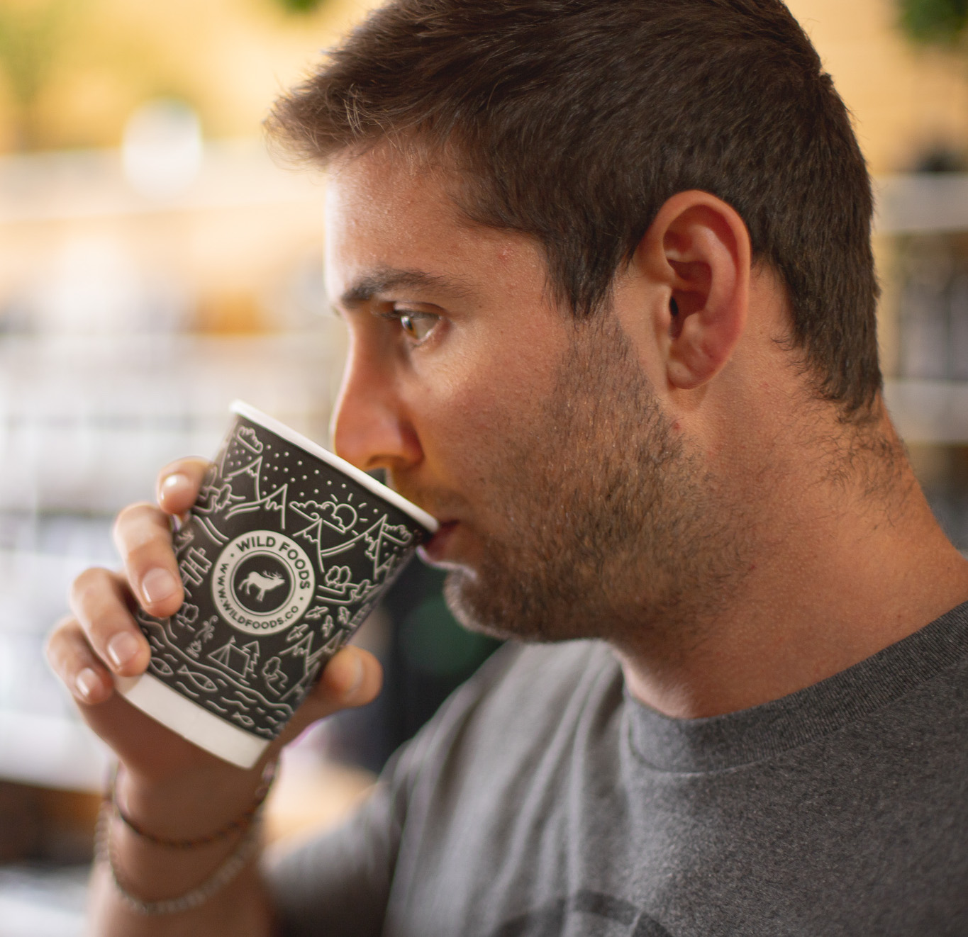 Man drinking from a decorated paper cup indoors.