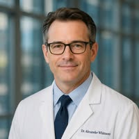 A headshot of a middle-aged man with glasses, wearing a white lab coat, shirt, and tie.