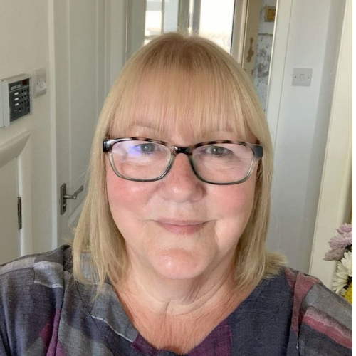 A close-up photo of a woman with blonde hair and glasses smiling at the camera.