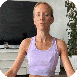 Person meditating indoors with eyes closed, wearing a purple tank top.
