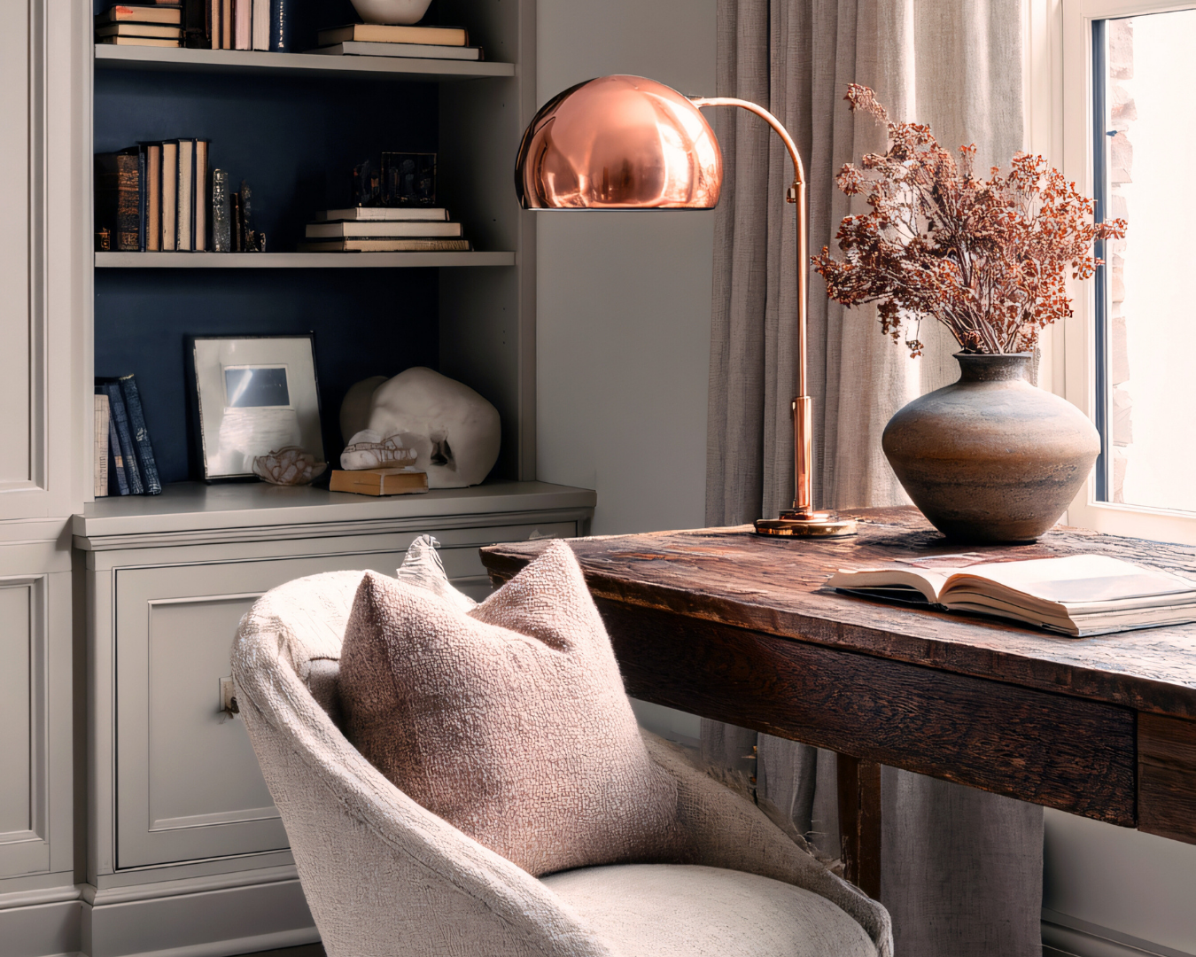 Cozy study with chair, desk lamp, bookshelves, and dried flowers in a vase.