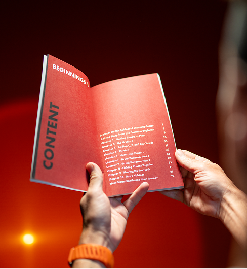 A person holds a red book open to the table of contents page against a red background.