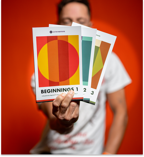 A person holds up three colorful Guitar Institute 'Beginnings' booklets, numbered 1, 2, and 3.