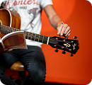 A person sits while tuning an acoustic guitar with a small book resting on the neck.