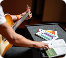 A person holds an acoustic guitar while looking at a music book on a stand.