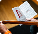 A person holds an instructional booklet while holding the neck of a guitar.