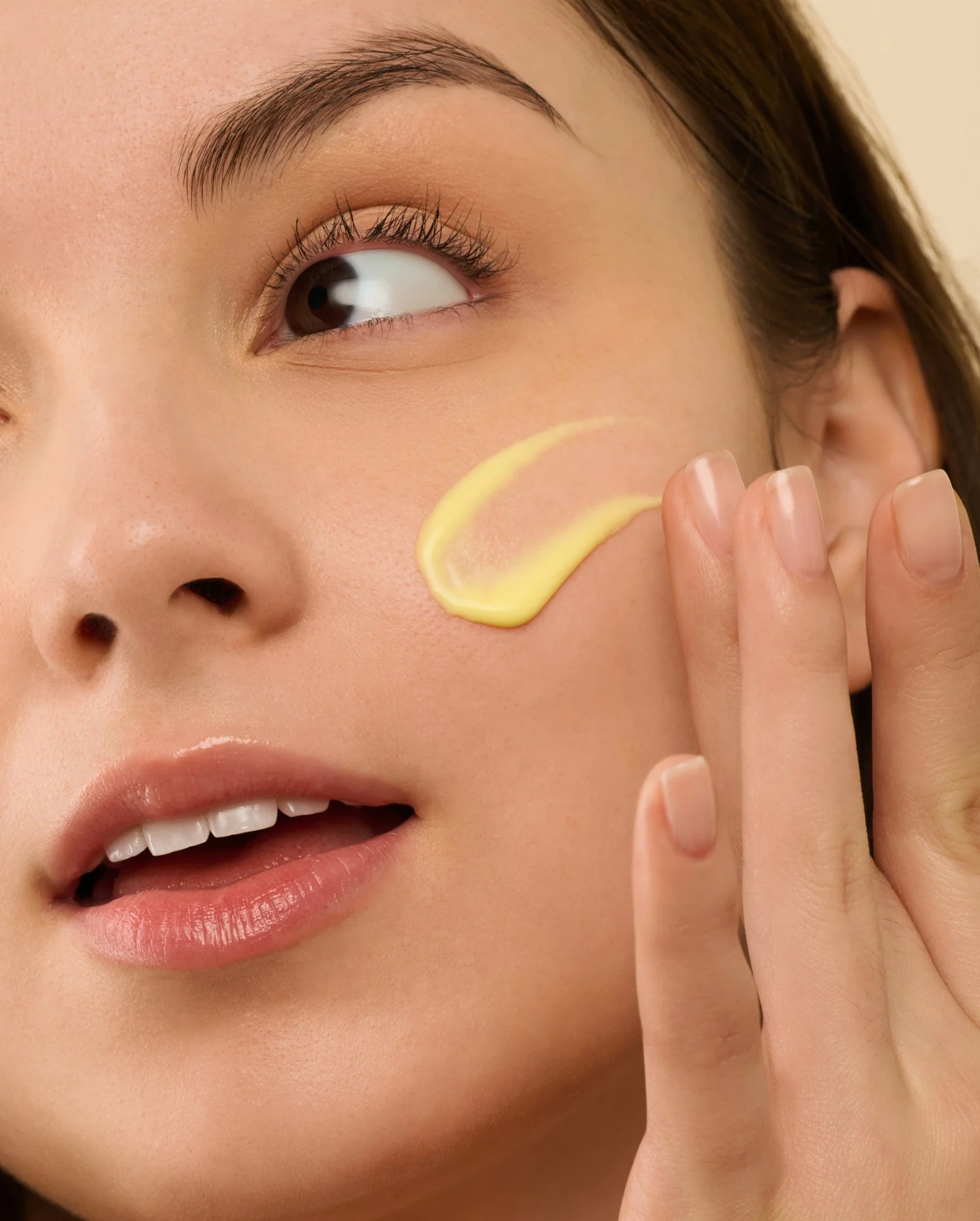 A person applying yellow cream to their cheek.