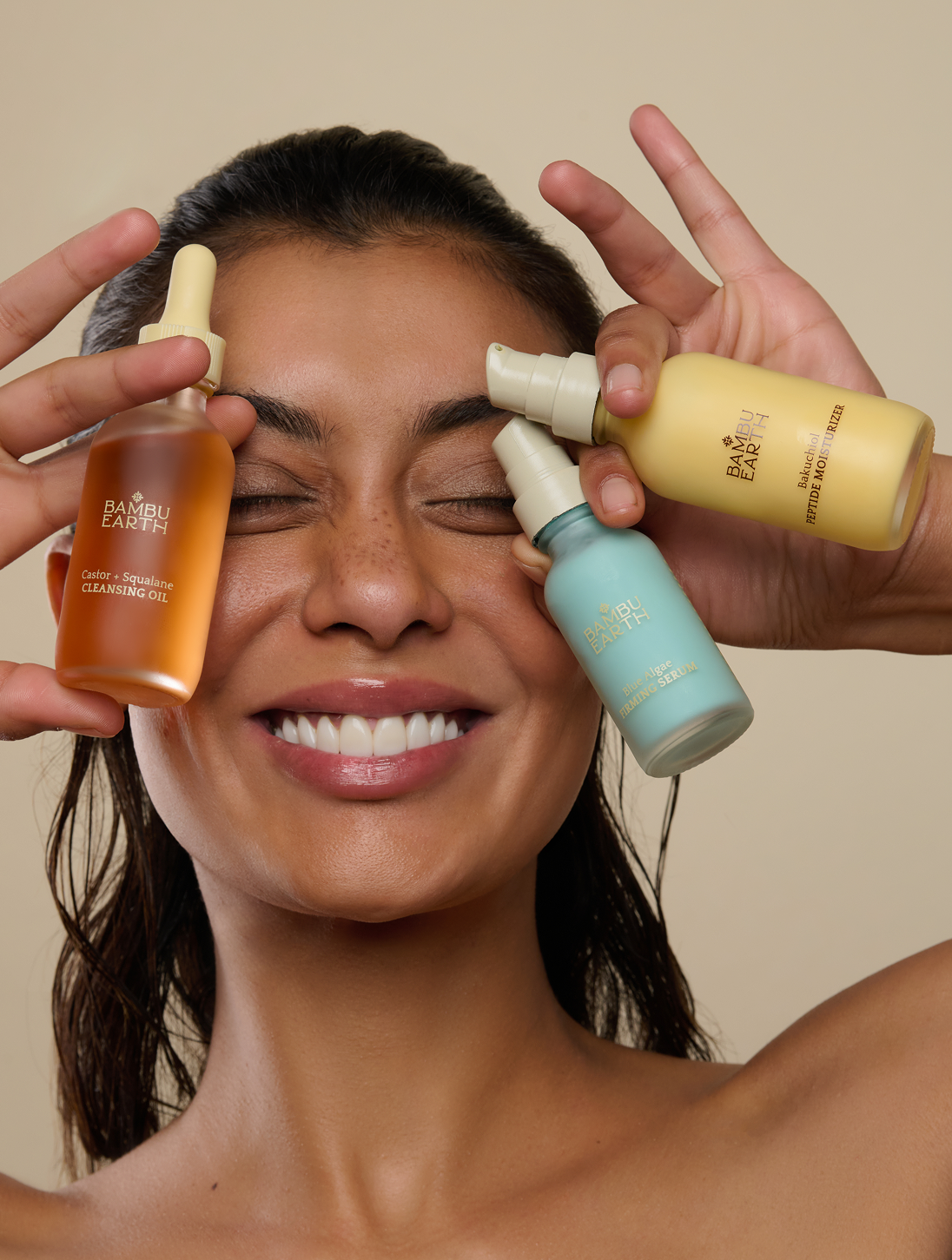 Smiling person holds three skincare product bottles near face.